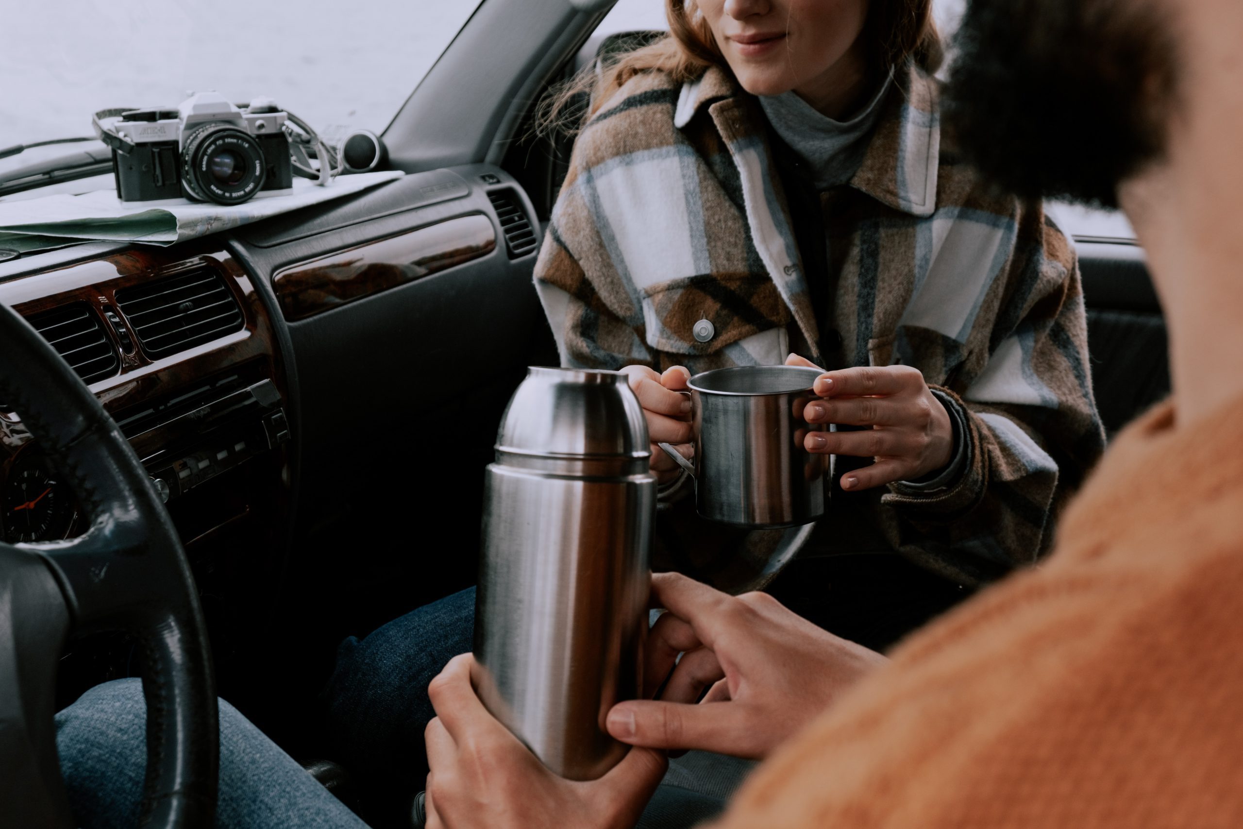 Podróżnicy nalewają sobie herbatę z termosa podczas podróży samochodem.